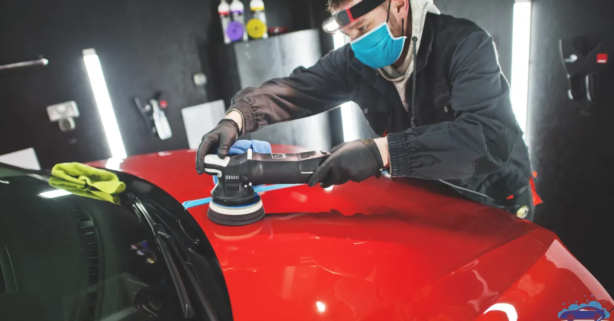 A professional detailer polishing a red car with a buffing machine in a well-lit workshop.