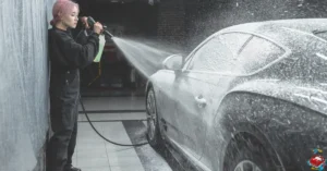 A person spraying foam onto a car in a detailing workshop, ensuring a thorough cleaning for the vehicle's exterior.