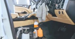 Close-up view of car interior detailing tools, including spray bottles, cleaning cloths, and equipment, in a beige and black vehicle.